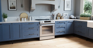 A kitchen with blue cabinets, white countertops, a stove, framed wall art, plants, and light wood flooring.