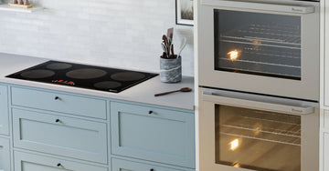 A modern kitchen with an induction cooktop and double wall ovens set within light-blue cabinetry, plus tiled backsplash.