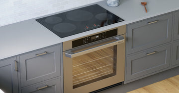 A stainless steel wall oven and black glass cooktop built into gray cabinets beneath a white tile backsplash.